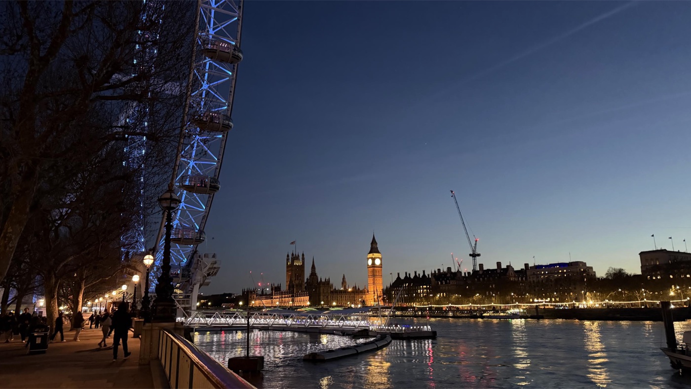 The London Eye lit blue beside the Houses of Parliament and Big Ben across the Thames at dusk