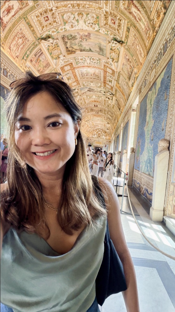 Portrait of Vivien Chin, smiling in a gallery beneath an ornate painted and gilded vaulted ceiling